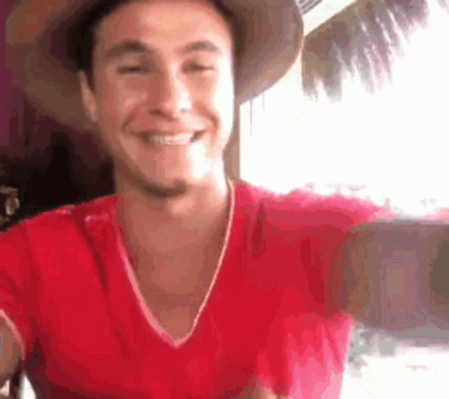a man in a red shirt and hat is smiling .
