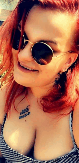 a woman with red hair is wearing sunglasses and has a tattoo on her chest that says ' a ' on it