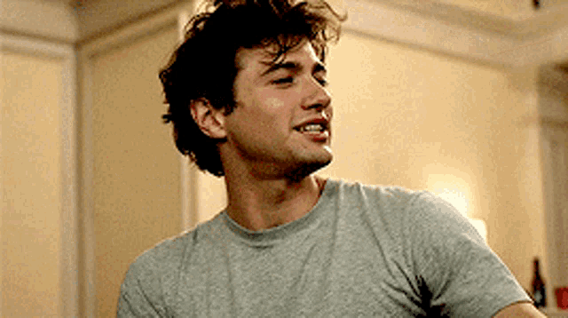 a man in a grey t-shirt is smiling and looking away from the camera