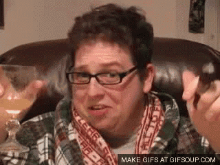 a man wearing glasses and a plaid shirt is sitting in a chair with a glass of wine .