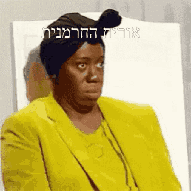 a woman in a yellow suit is sitting in a chair with hebrew writing behind her