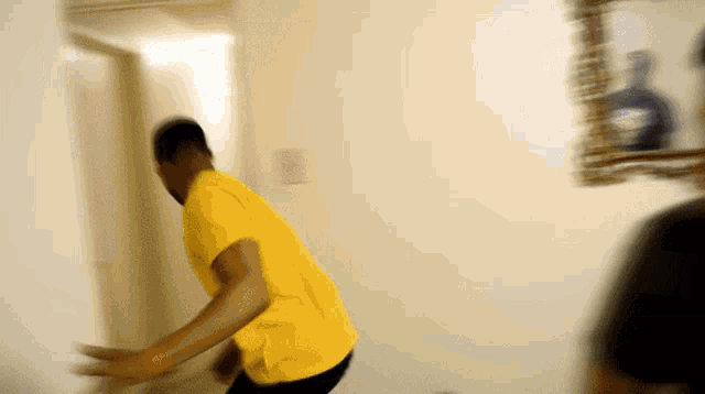 a man in a yellow shirt is standing in front of a white wall