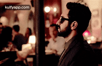 a man with a beard and sunglasses is standing in a crowded room .