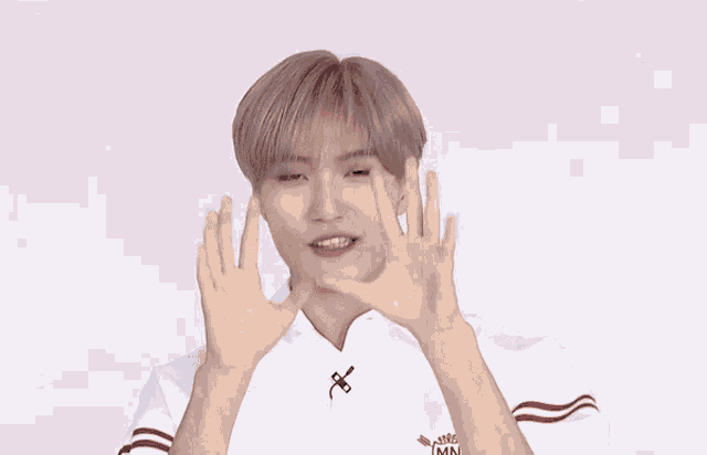 a young man wearing a white shirt with red stripes on the sleeves is making a heart shape with his hands