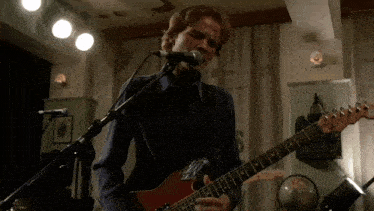 a man singing into a microphone while playing a red guitar