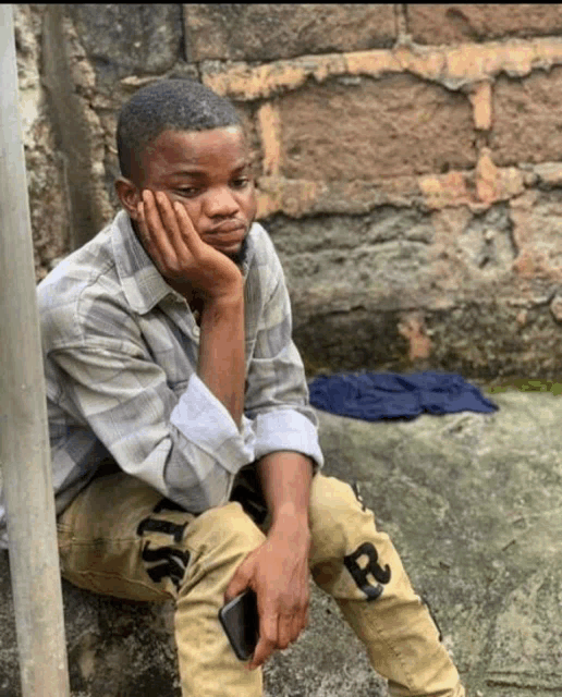 a young man sitting on the ground with his hand on his chin
