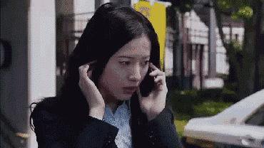 a woman in a suit is talking on a cell phone while covering her ears .