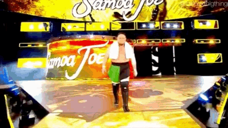 a wrestler is walking on a stage in front of a sign that says samoa joe