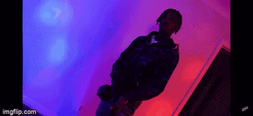 a man is standing in a room with a purple and blue light behind him .