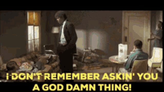 a man in a suit is standing in a living room next to a woman laying on a couch .