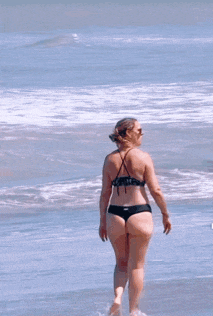 a woman in a bikini is standing on a beach looking at the ocean