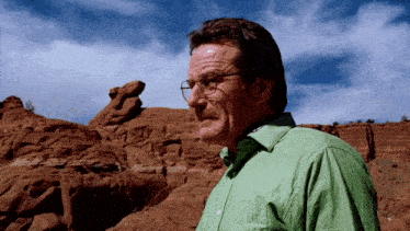 a man wearing glasses and a green shirt stands in a desert