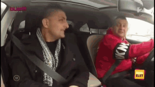 two men are sitting in a car and one of them is wearing a knk sweater