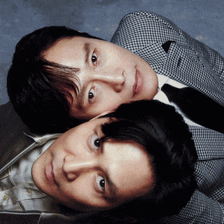two men laying on top of each other with one wearing a plaid suit and tie