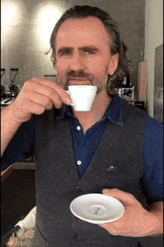 a man with a beard is drinking from a cup on a saucer