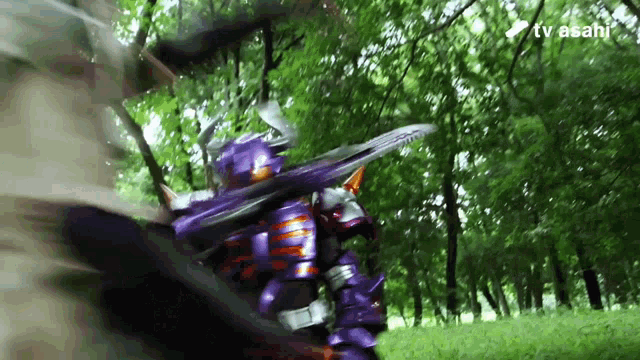 a man in a purple armor is fighting another man in a forest with a tv asahi logo in the background
