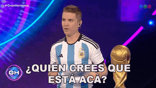 a man in a soccer jersey stands next to a trophy and says quien crees que esta aca