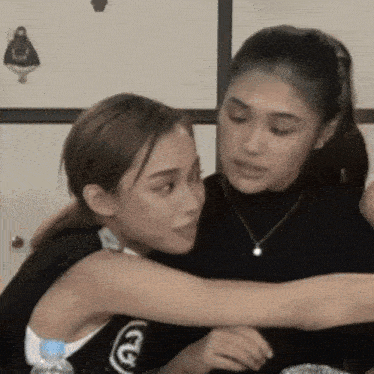 two women are hugging each other and one has a bottle of water in her hand .