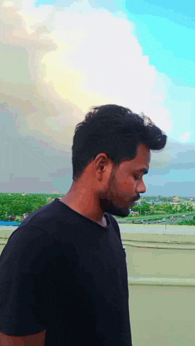 a man with a beard and a black shirt is standing on a rooftop looking down .