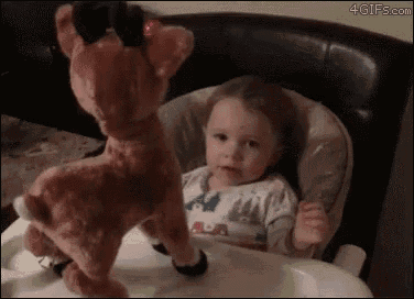 a little girl is sitting in a high chair with a stuffed reindeer .