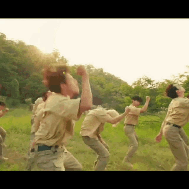 a group of people are dancing in a field with the sun shining through the trees behind them