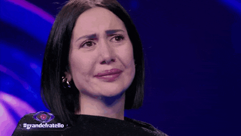 a woman is crying on a stage in front of a blue background with the words grandefratello on it .
