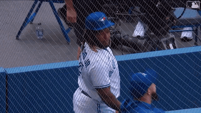 a man in a blue jays jersey stands behind a chain link fence