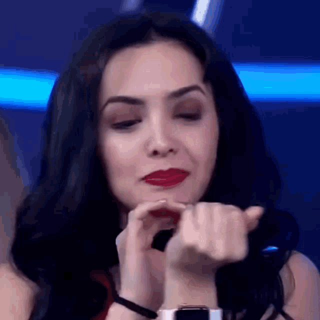 a woman with red lipstick and a watch on her wrist is making a heart with her hands .