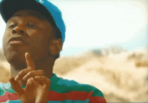 a man wearing a blue hat and a striped shirt is making a peace sign with his hands .