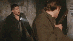 a man is holding a flashlight in a dark room while another man stands behind him .