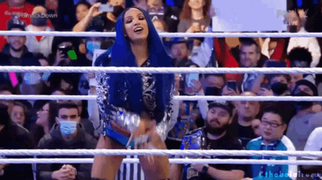 a woman with blue hair is standing in a wrestling ring with a crowd behind her .
