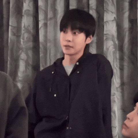 a young man in a black jacket is standing in front of a curtain and looking at something .