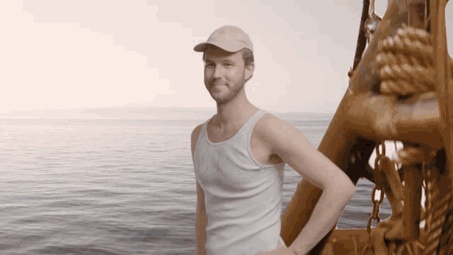a man wearing a white tank top and a pink hat is standing on a boat in the ocean