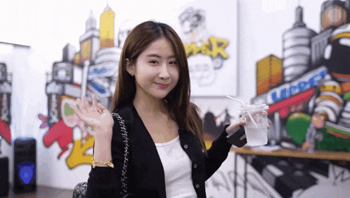 a woman holding a drink in front of a wall with graffiti that says ' mar ' on it