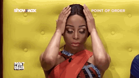 a woman in a red dress is covering her head with her hands while sitting on a yellow couch .