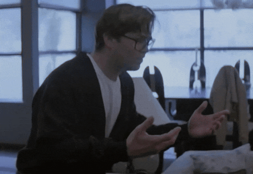 a man wearing glasses is sitting at a table with his hands out