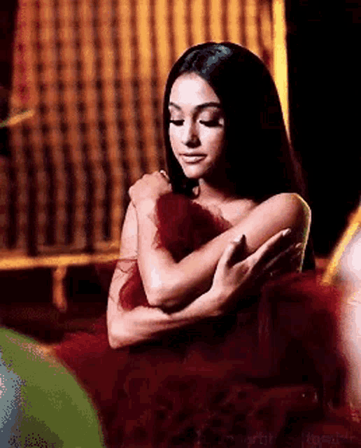 a woman in a red dress is hugging herself with her arms around her chest .