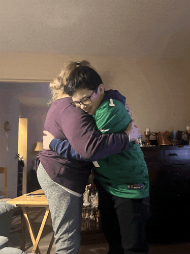 a boy in a green jacket with the number 1 on it is hugging a woman in a purple shirt