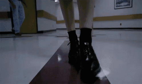 a woman wearing black boots is standing on a staircase in a hallway .