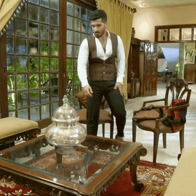 a man in a brown vest and white shirt stands in a living room