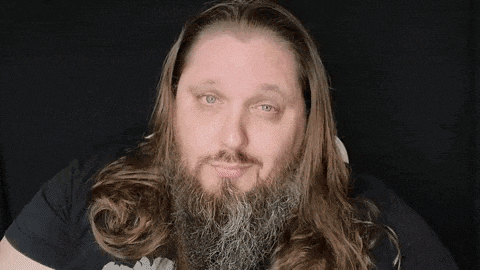 a man with long hair and a beard is looking at the camera and smiling .