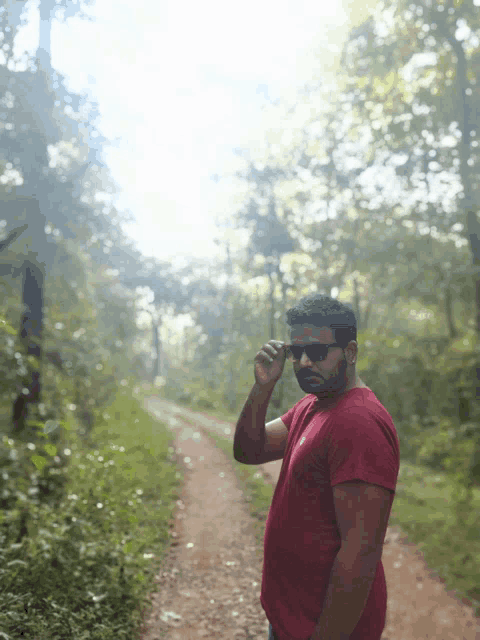 a man wearing sunglasses and a red shirt is standing on a dirt road