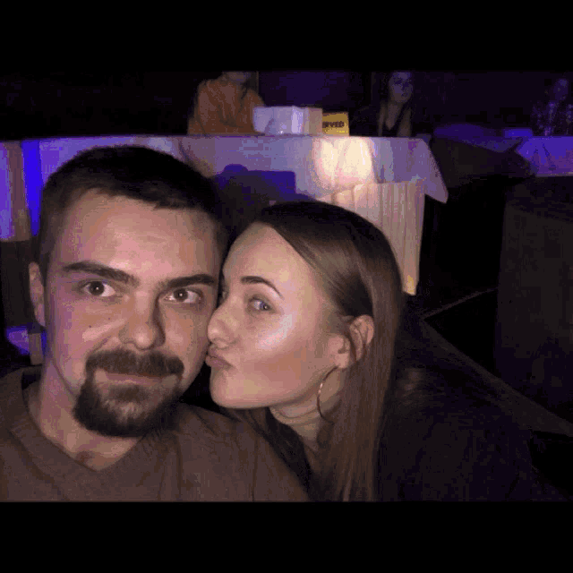 a woman kisses a man on the cheek in a dark room with a yellow sign that says svid