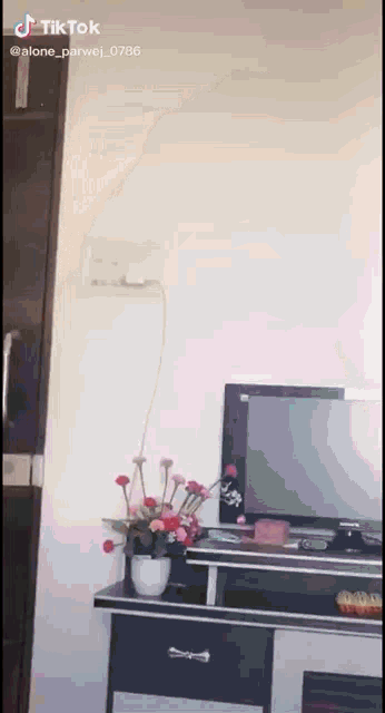 a tv sitting on top of a desk next to a vase of flowers .