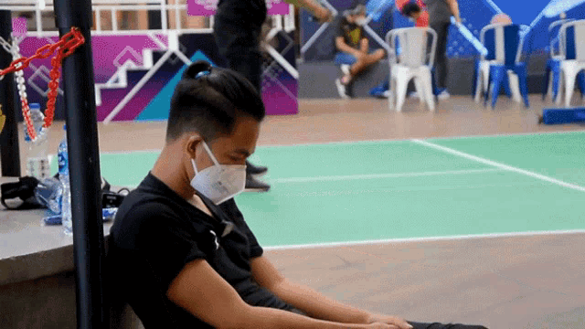 a man wearing a mask sits on the floor in a gym
