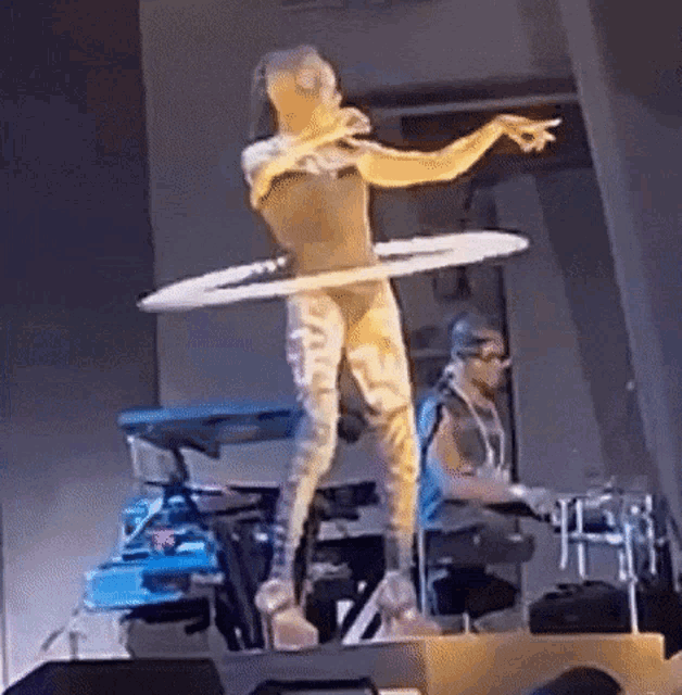 a woman is dancing with a hula hoop on a stage while a man plays drums behind her