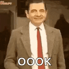 mr bean is wearing a suit and tie and smiling while standing in front of a mirror .