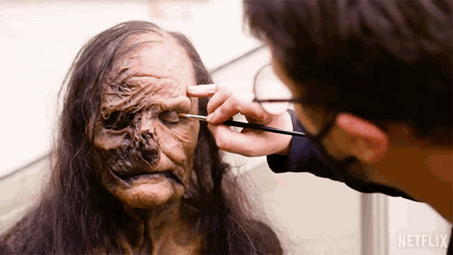 a person is applying makeup to another person 's face with a netflix logo on the bottom right