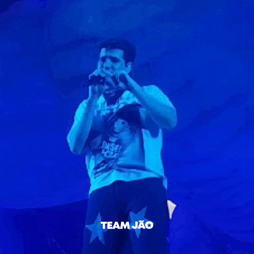 a man is singing into a microphone while wearing a shirt that says team jao .