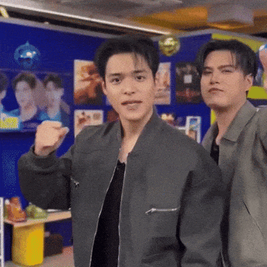 two men are standing next to each other in a room . one of the men is wearing a bomber jacket .